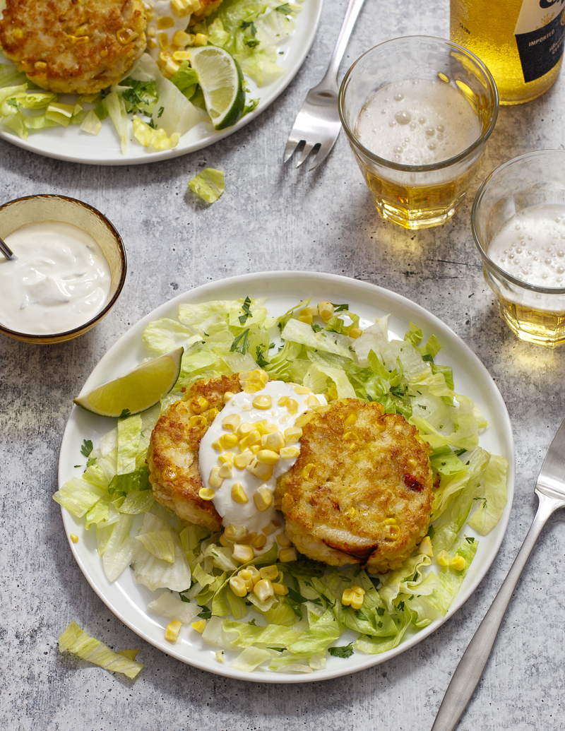 Corn and Crab Cakes with Cilantro and Lime Sour Cream / JillHough.com Corn—both in the cakes and as a garnish—along with cilantro, lettuce, and lime, gives this classic a slight Tex-Mex spin. On the side, serve tortilla chips to scoop up every mouthful. #corn #crabcakes #cilantro #lime #cornandcrab #corncakes